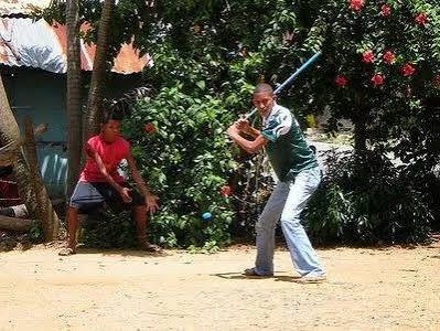 Jóvenes jugando vitilla con una tapa plástica y un palo en un espacio abierto de la República Dominicana.
